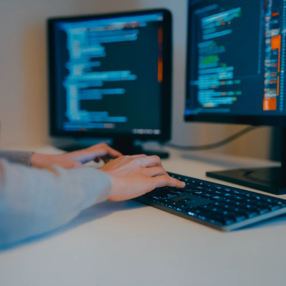 Person typing code on computer with survey automation scripts on screen