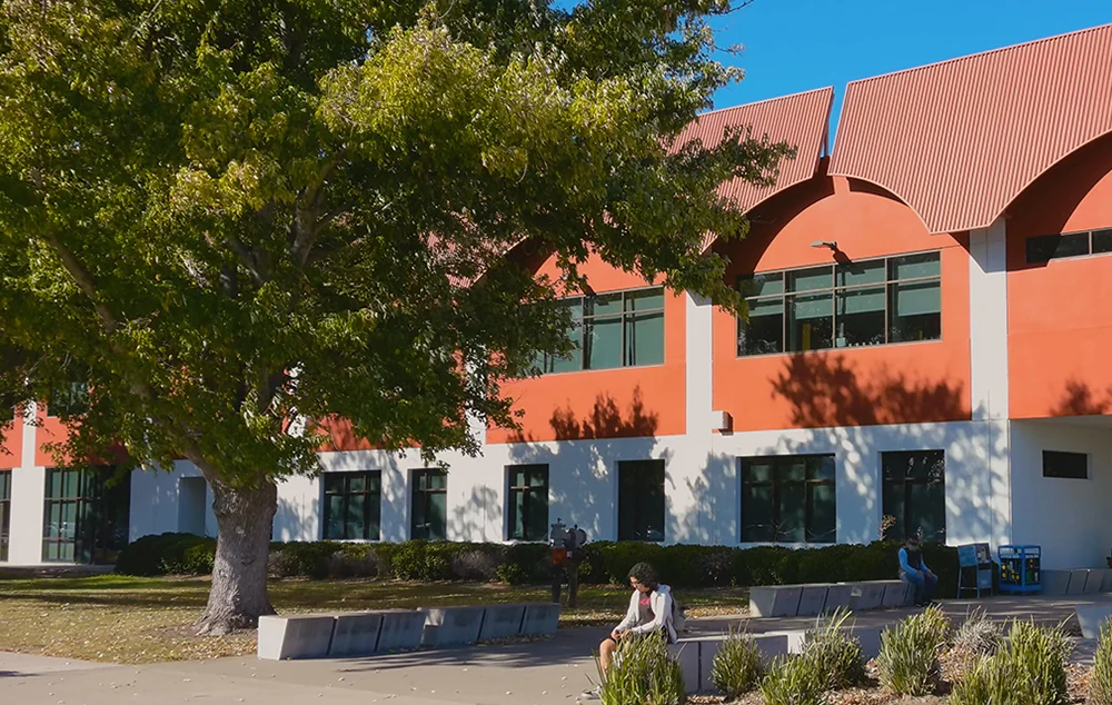 Modern college campus building with students sitting outside on a sunny day